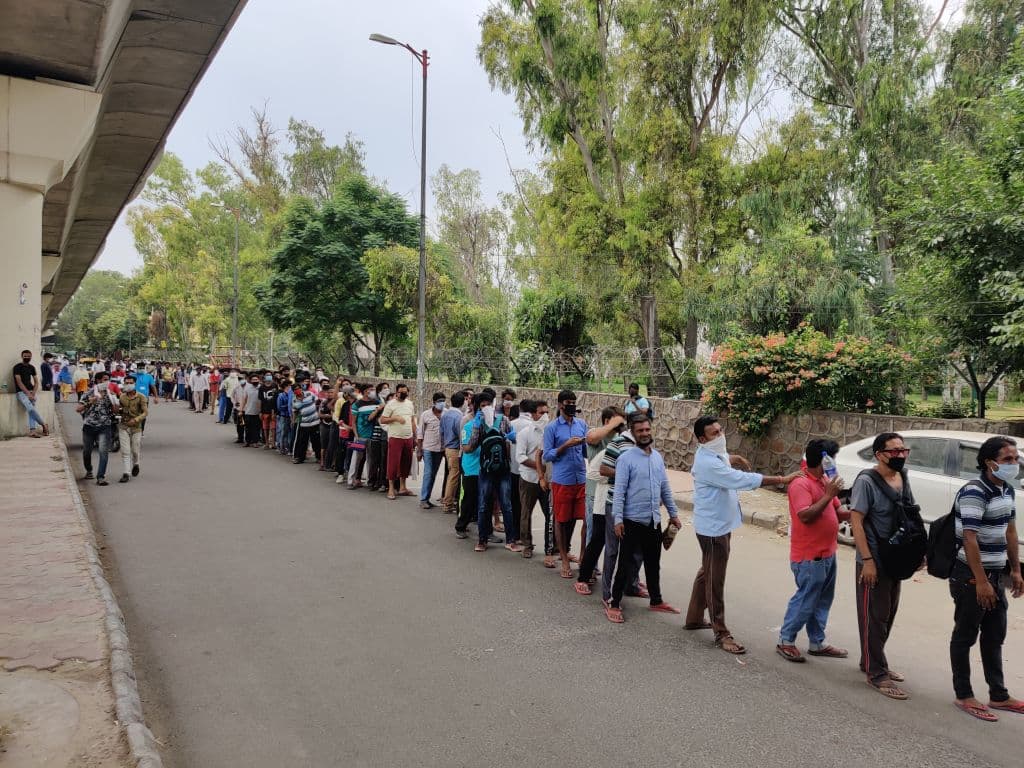 Todos en esta enorme cola (o fila, como prefieras llamarle) esperan para comprar alcohol, en Nueva Delhi, India, el problema es que hay demasiada cercanía entre las personas formadas. El momento es del 6 de mayo de 2020, y el gobierno de Delhi impuso un impuesto especial del 70% sobre las compras de alcohol para disuadir las reuniones en las tiendas por el cierre de seis semanas.